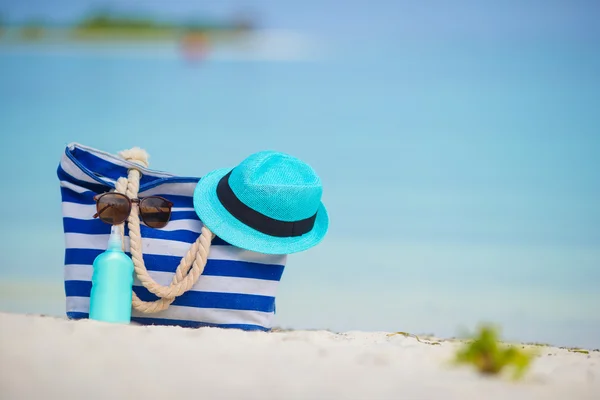 Blue bag, straw hat, sunglasses and sunscreen bottle on white beach — Stock Photo, Image