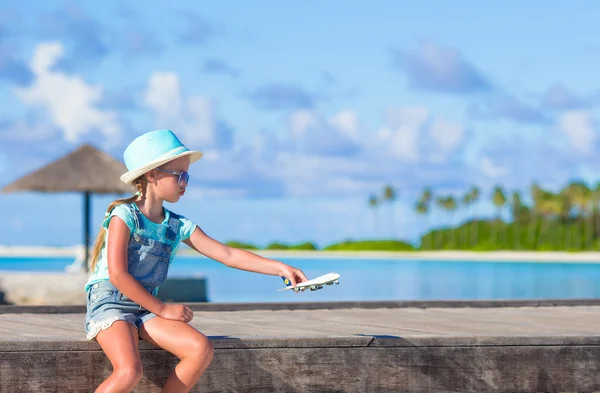 Счастливая маленькая девочка с игрушечным самолетом в руках на белом песчаном пляже — стоковое фото