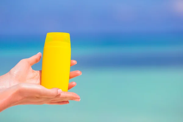 Kvinnliga händer med solkräm flaska bakgrunden blå havet — Stockfoto