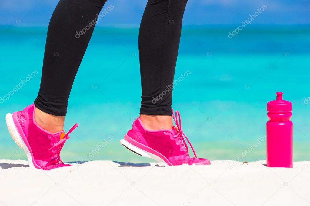 Close-up of female legs in sneakers running on white sandy beach