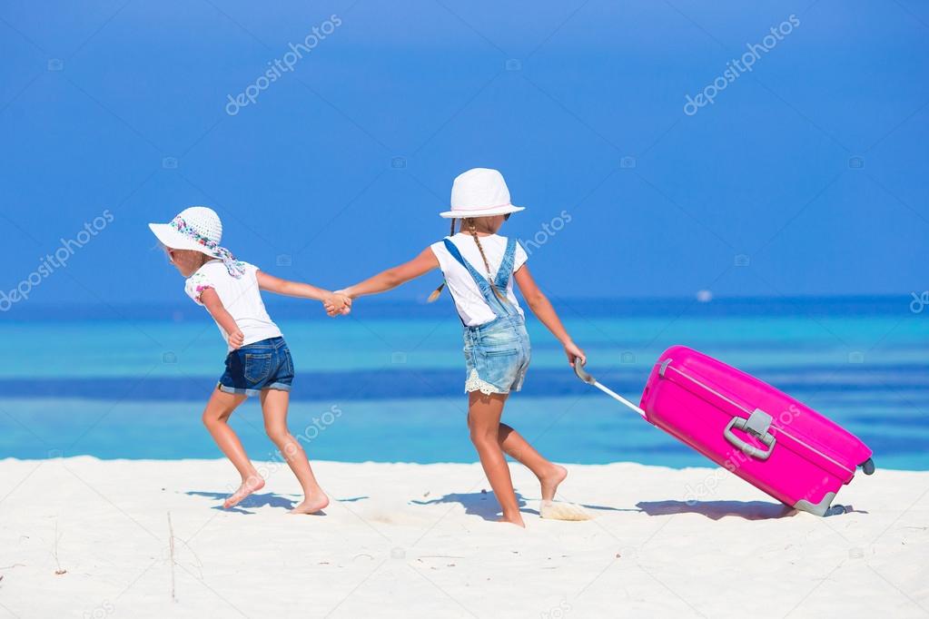 Little adorable girls with big suitcase on tropical white beach during summer vacation