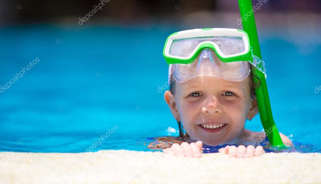 Adorable little girl at mask and goggles in outdoor swimming pool