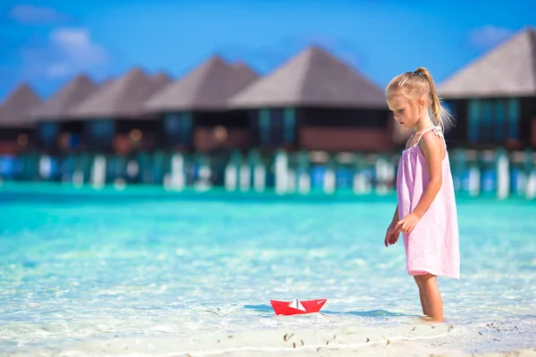 Adorable little girl playing with paper boat in turquoise sea — Stock Photo, Image