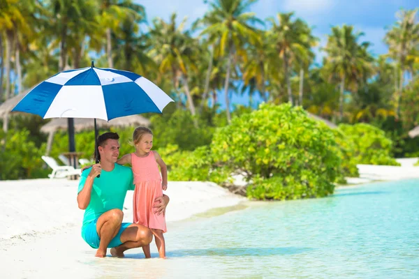 Father and little girl with umbrella hiding from sun at beach — Stock Photo, Image