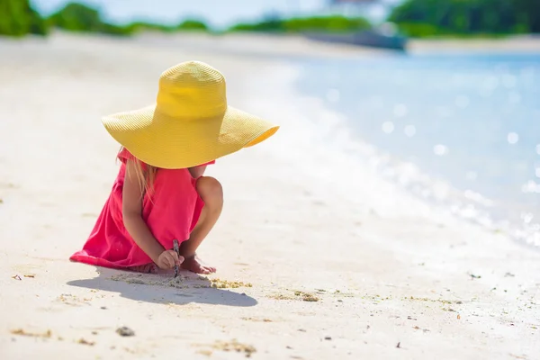 Красивая маленькая девочка рисует на белом песке на пляже — стоковое фото