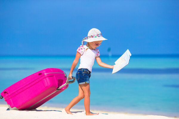 Little adorable girl with big suitcase on tropical white beach