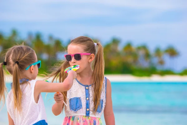 Zwei kleine Mädchen essen helle Lutscher am Strand — Stockfoto