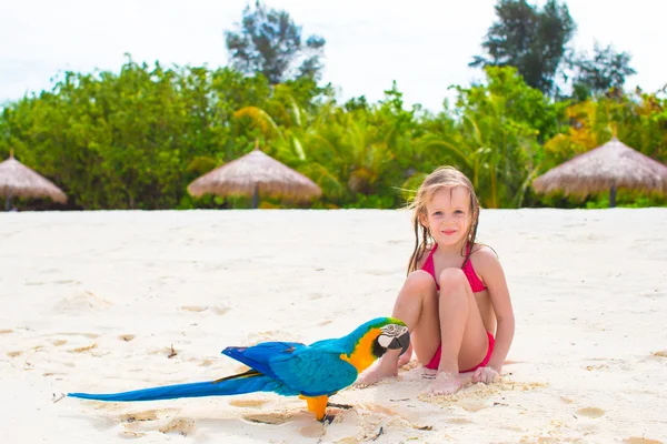 Adorable little girl at beach with colorful parrot — Stock Photo, Image