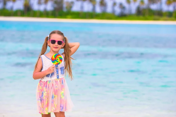 Adorable little girl with lollipop on tropical beach — Stock Photo, Image