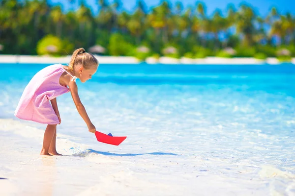 Bedårande liten flicka spelar med papper båt i turkosa havet — Stockfoto