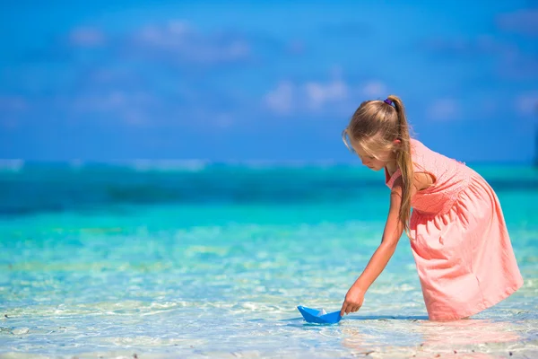 Adorable little girl playing with origami boat in turquoise sea — Stock Photo, Image