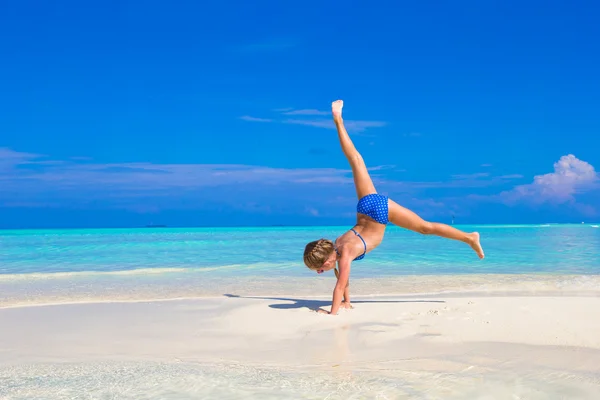 Adorable little girl having fun making cartwheel on tropical white sandy beach — Stock Photo, Image