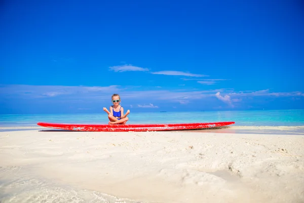 Petite fille en position de yoga méditant sur planche de surf — Photo