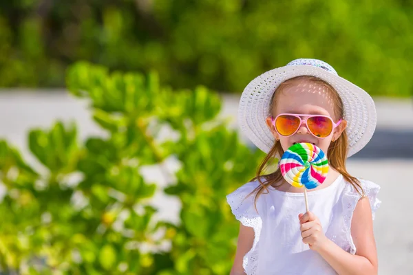 Adorable little girl with lollipop on tropical beach — Stock Photo, Image