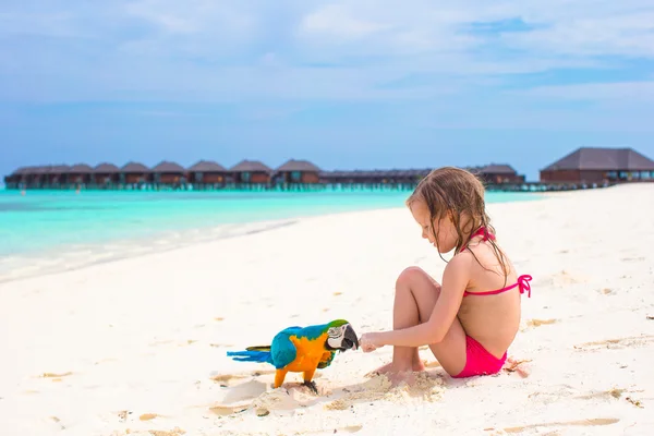 Adorable little girl at beach with colorful parrot — Stock Photo, Image