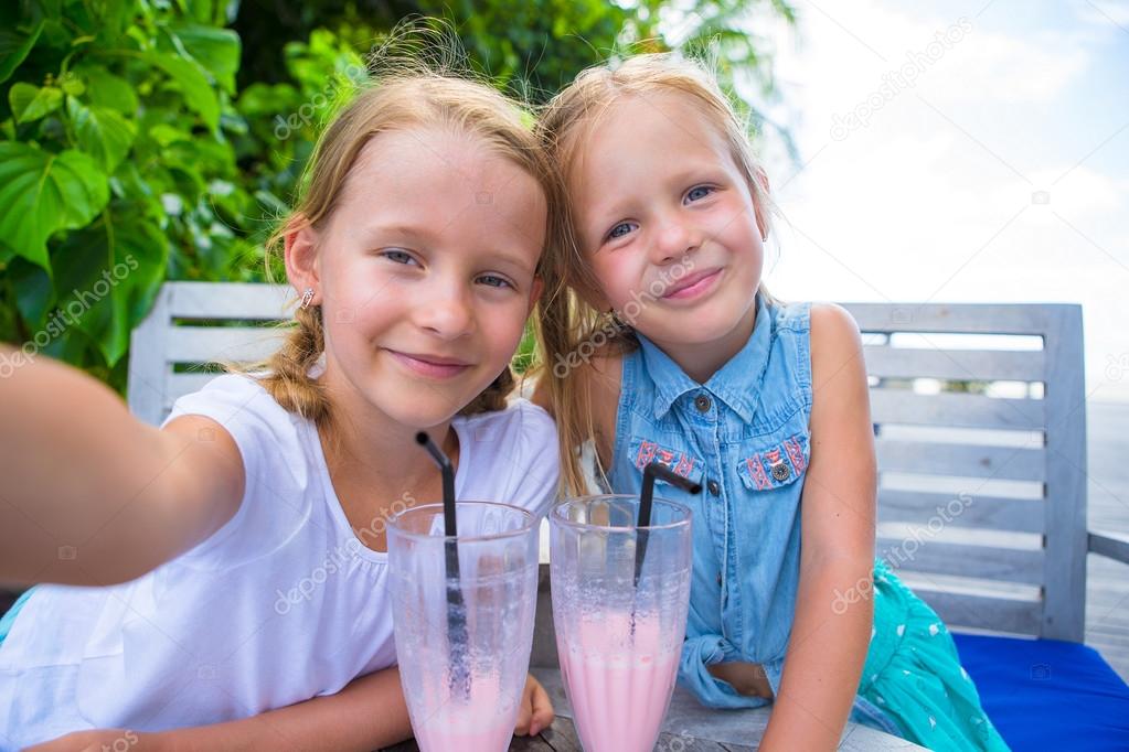 Little girls taking selfie and drinking tasty cocktails at tropical resort