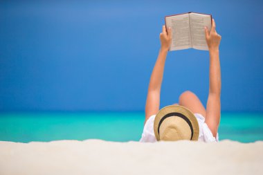 Genç kadın tropikal beyaz plajda kitap okuyor.