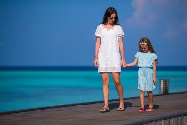 Niña y madre joven caminando en un embarcadero de madera en un resort exótico — Foto de Stock