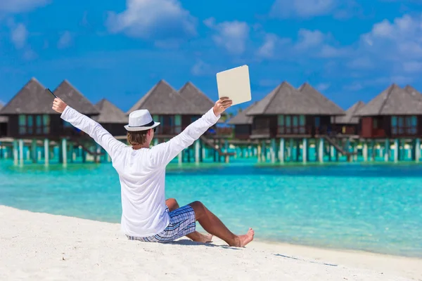 Young man with laptop at tropical beach near water villa — Stock Photo, Image