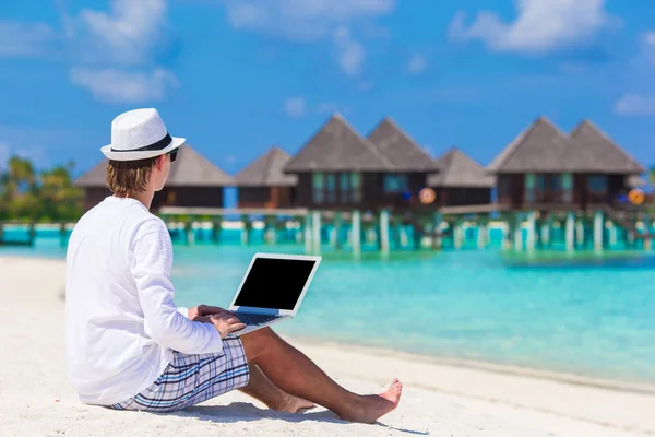 Young man with laptop at tropical beach near water villa — Stock Photo, Image
