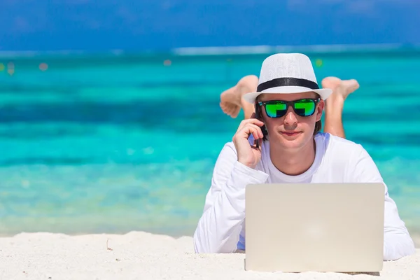 Jonge man met tablet pc en mobiele telefoon op tropisch strand — Stockfoto