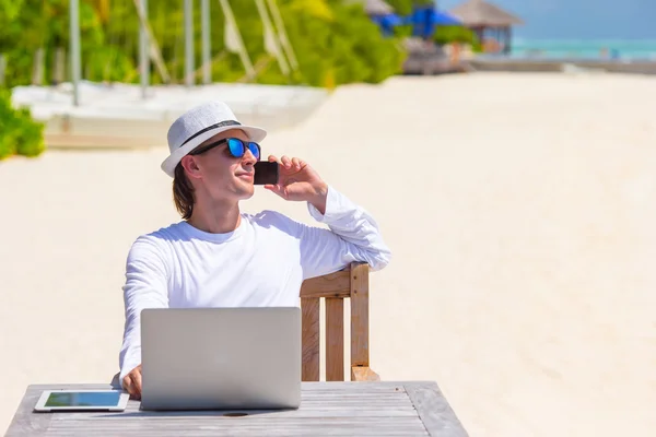 Ung man med handdator och mobiltelefon på tropical beach — Stockfoto