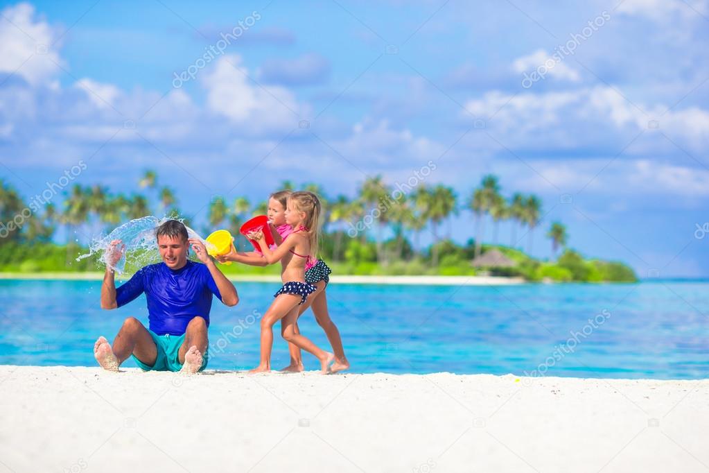 Adorable little girls having fun with dad on white beach