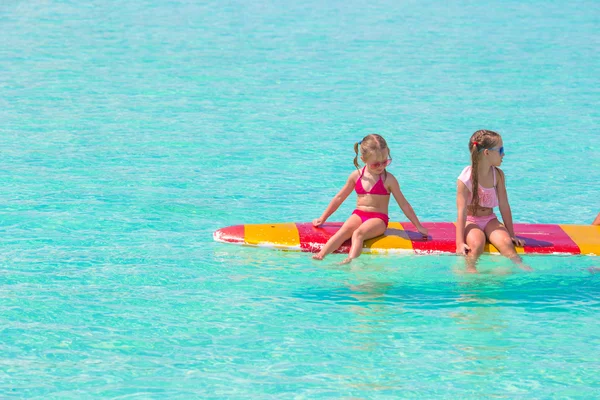 Little adorable girls on a surfboard in the turquoise sea — Stock Photo, Image