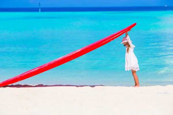 Adorable petite fille avec une grande planche de surf rouge sur une plage blanche tropicale — Photo