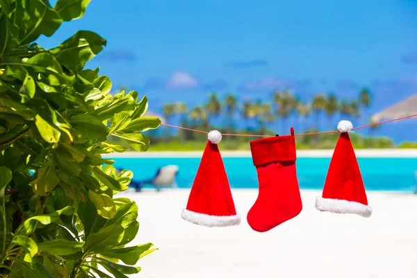 Red Santa hats and Christmas stocking hanging on tropical beach — Stock Photo, Image