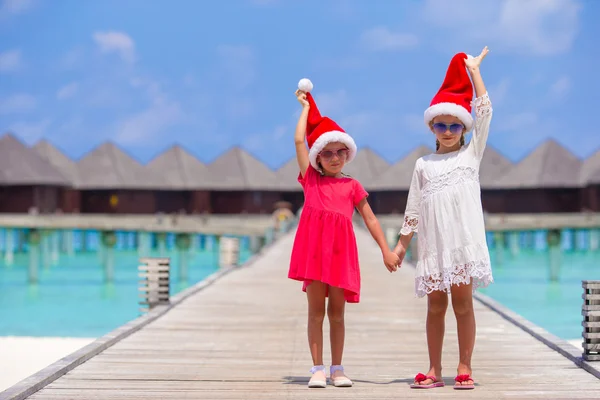 Kleine entzückende Mädchen mit Weihnachtsmützen während des Strandurlaubs am Holzsteg — Stockfoto