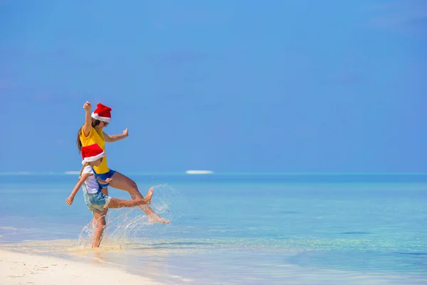 Kleines Mädchen und junge Mutter mit Weihnachtsmann im Strandurlaub — Stockfoto