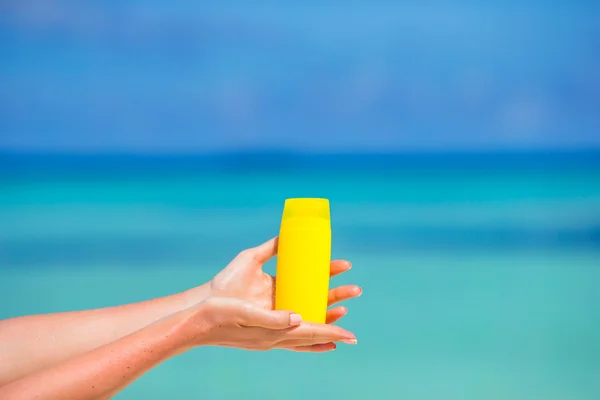 Mani femminili con crema solare bottiglia sfondo blu mare — Foto Stock