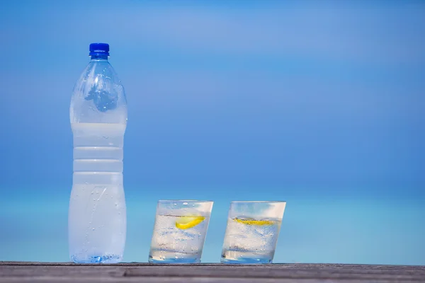 Glazen water met citroen en fles op houten op zee achtergrond — Stockfoto