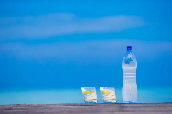 Glazen water met citroen en fles op houten op zee achtergrond — Stockfoto