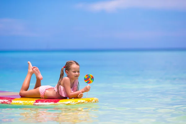 Little girl with lollipop have fun on surfboard in the sea — Stock Photo, Image