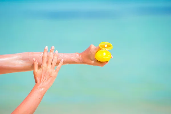 Manos femeninas con crema solar botella fondo azul mar — Foto de Stock