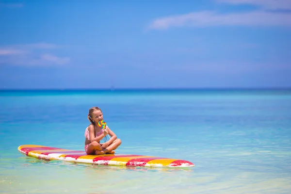Kleines Mädchen mit Lutscher hat Spaß auf Surfbrett im Meer — Stockfoto