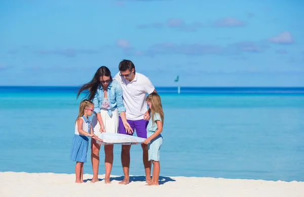 Familia joven feliz de cuatro con mapa en la playa — Foto de Stock