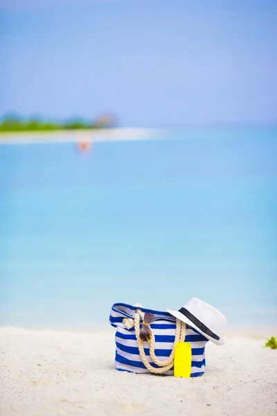 Bolso azul, sombrero de paja, gafas de sol y botella de protector solar en la playa blanca — Foto de Stock