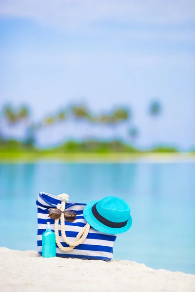 Blue bag, straw hat, sunglasses and sunscreen bottle on white beach — Stock Photo, Image