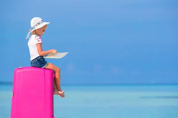 Little adorable girl with big pink suitcase and map on white beach — Stock Photo, Image