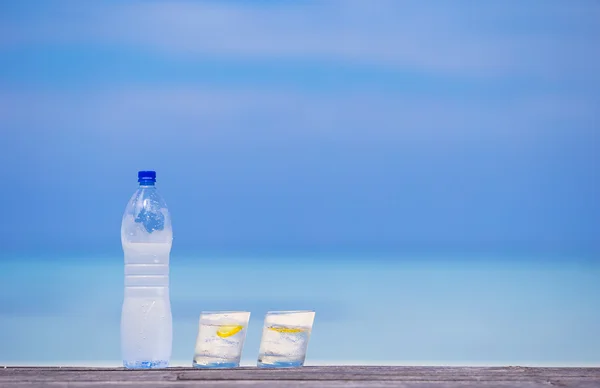 Glazen water met citroen en fles op houten op zee achtergrond — Stockfoto