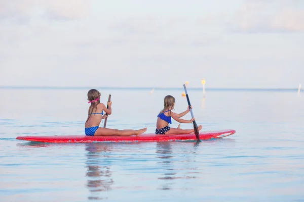 Kleine süße Mädchen schwimmen in den Sommerferien auf dem Surfbrett — Stockfoto