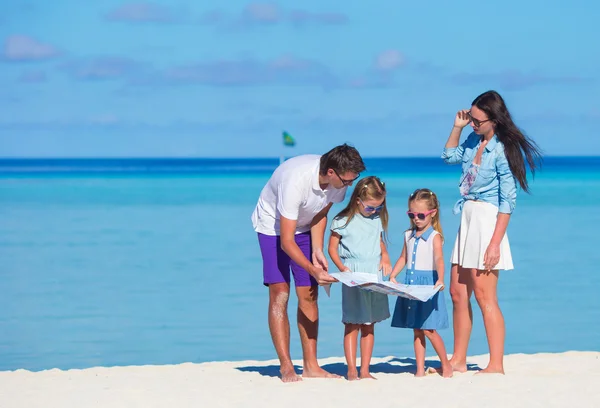 Glad ung familj av fyra med karta på stranden — Stockfoto