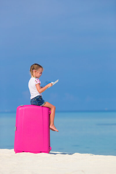 Little adorable girl with big pink suitcase and map of island on white beach