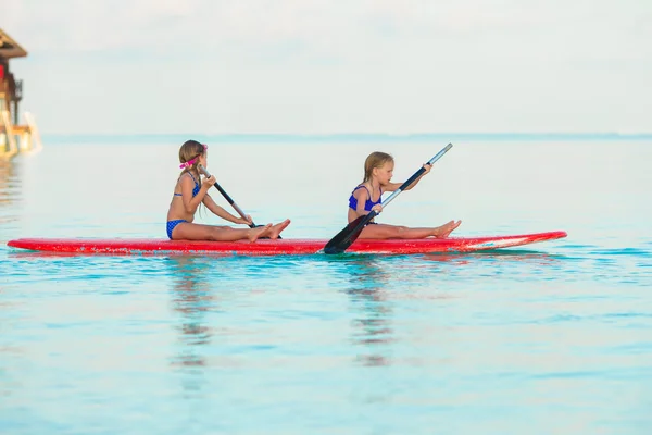 Piccole ragazze carine che nuotano sulla tavola da surf durante le vacanze estive — Foto Stock