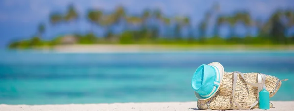 Straw bag, blue hat, sunglasses and sunscreen bottle on tropical beach — Stock Photo, Image
