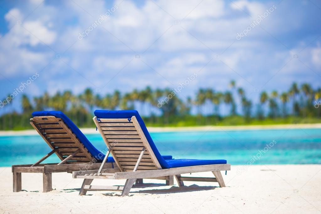 Lounge chairs with bag and hat on tropical white beach