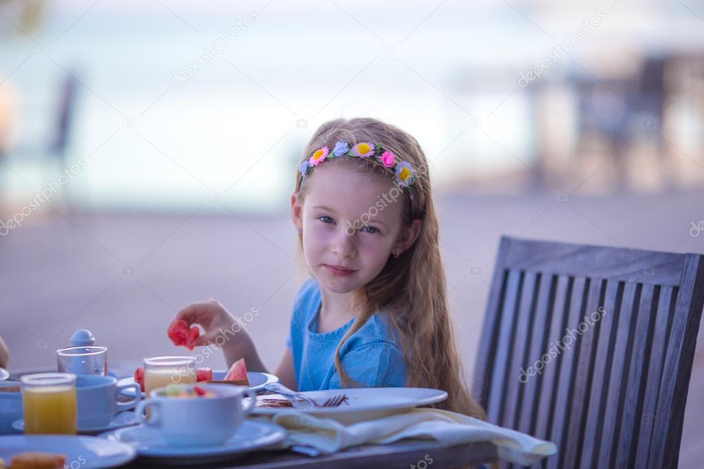 Adorable little girl having breakfast at outdoor cafe
